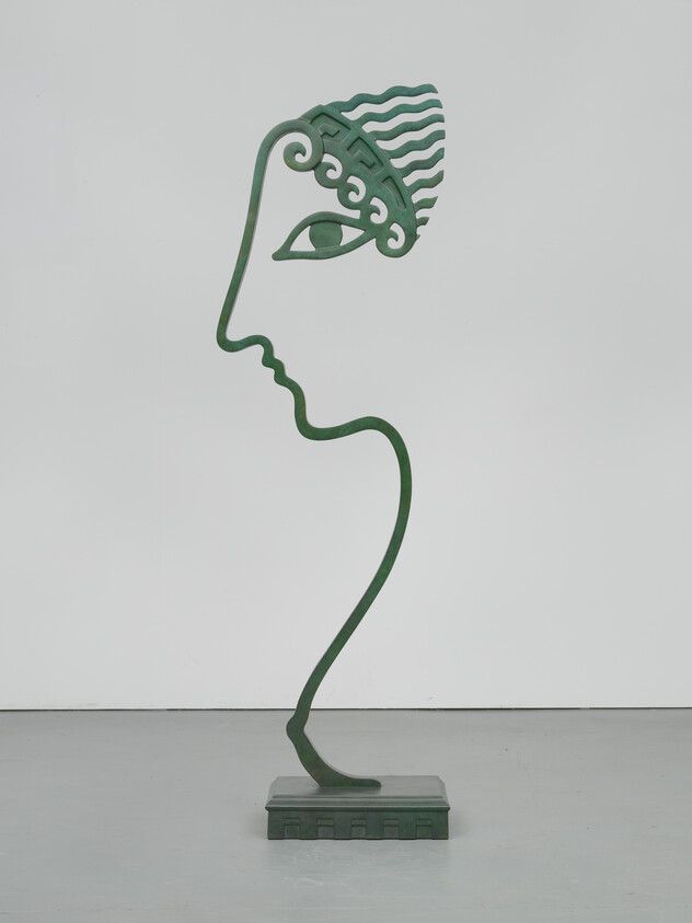 A tall green metal outline sculpture depicts a stylized human profile mounted on a square base.