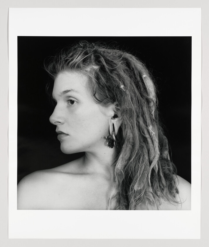 Young woman with long dreadlocks in profile wearing multiple earrings and bare shoulders.