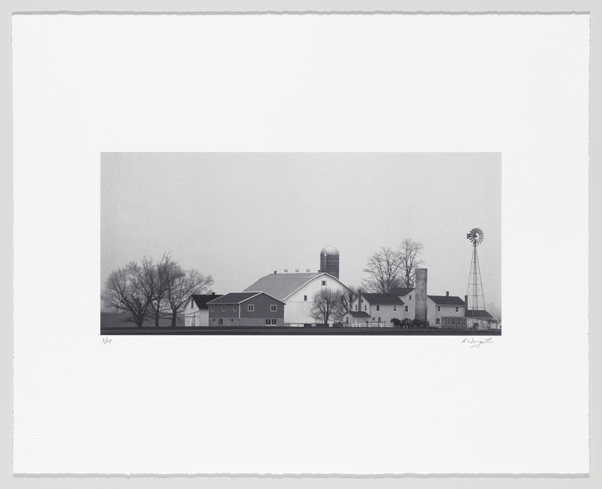 Black and white photograph of a rural farm scene with a silo, barn, windmill, and bare trees under a hazy sky, with the image framed by a wide white border containing signatures and edition number on the bottom.