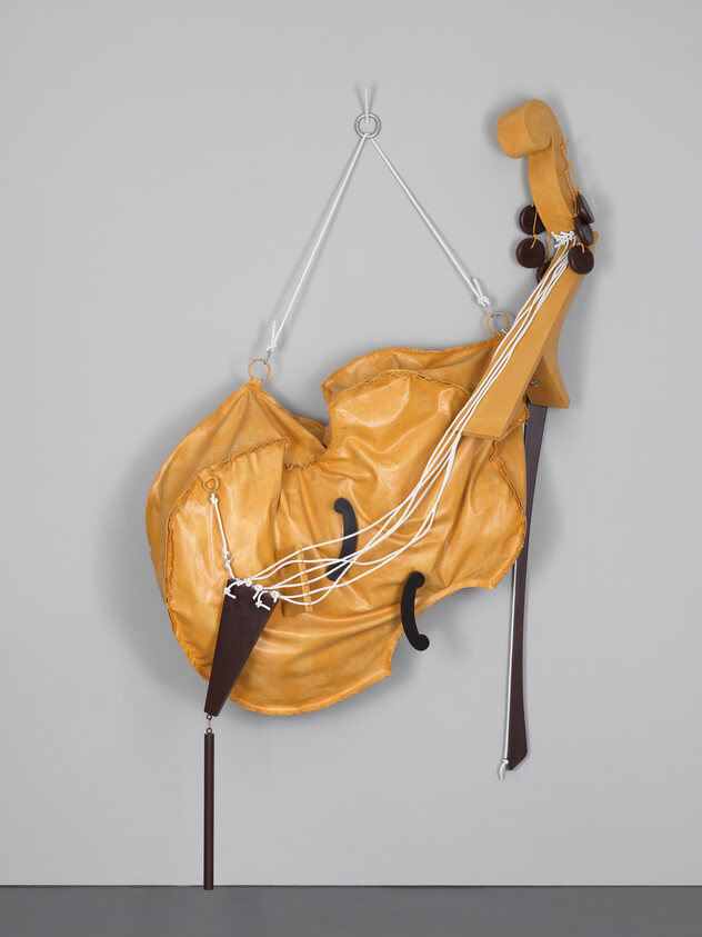Yellow leather sculpture resembling a deformed cello suspended from metal hooks with white cords.