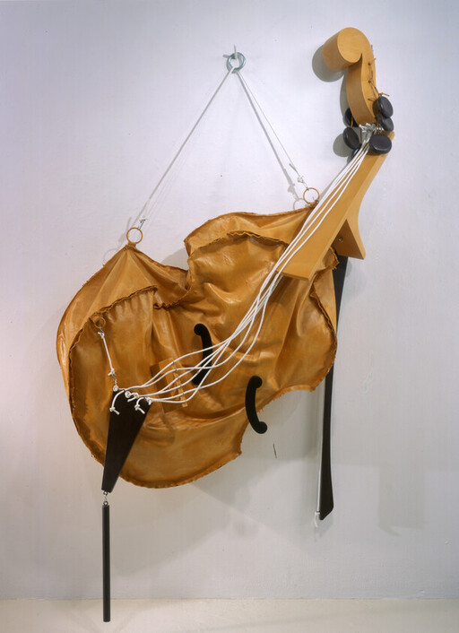 Yellow leather sculpture resembling a deformed cello suspended from metal hooks with white cords. — view 104641