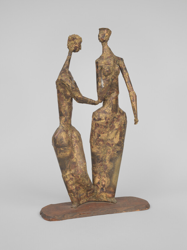 Two tall abstract metal figures stand close together and hold hands on a flat base.