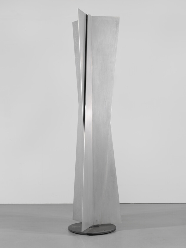 Tall abstract metal sculpture made of twisted vertical panels standing on a round base.