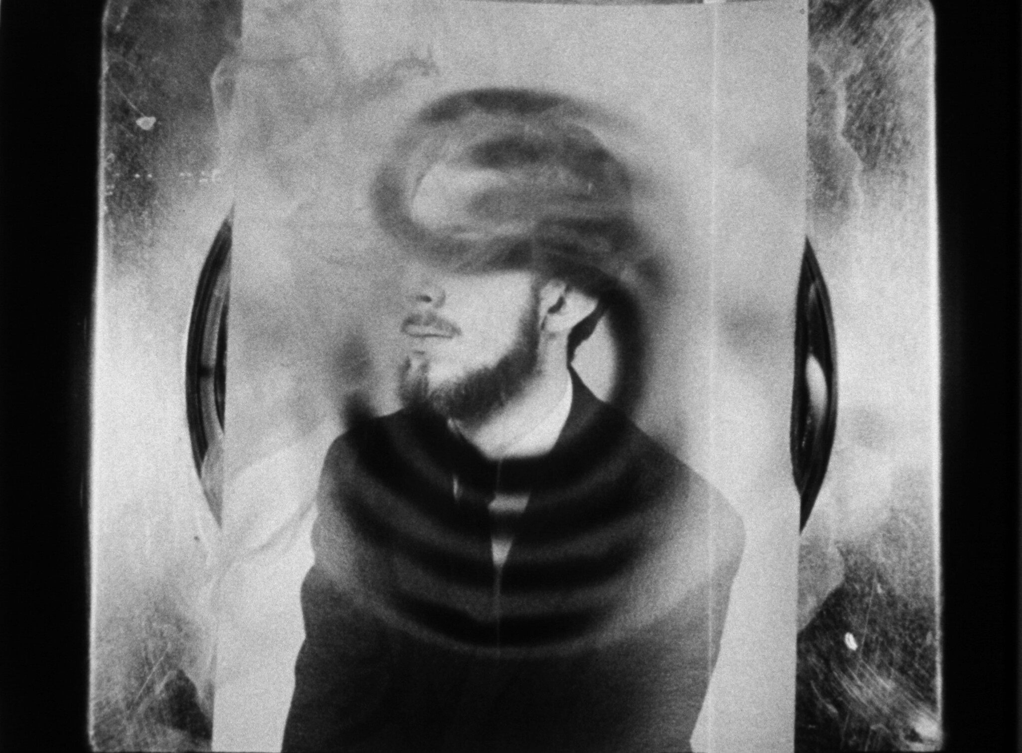 Bearded man looks left as circular ripple patterns distort his face and chest.