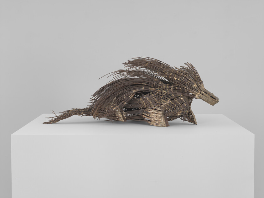 A wooden stick sculpture resembling a porcupine rests on a white pedestal.