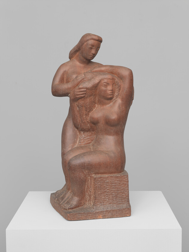 Two women in a terracotta sculpture, one seated while the other arranges her hair.