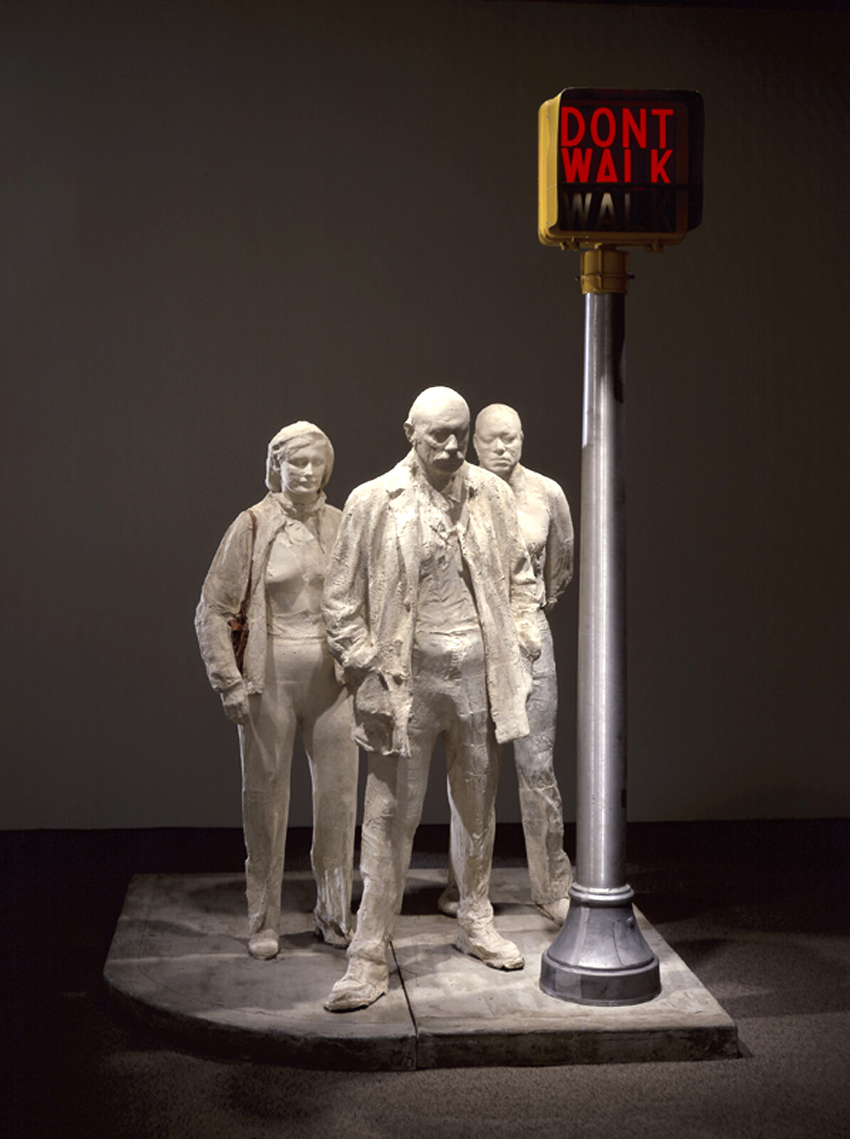 Three white sculpted figures stand under a lit pedestrian sign that reads "Don't walk."