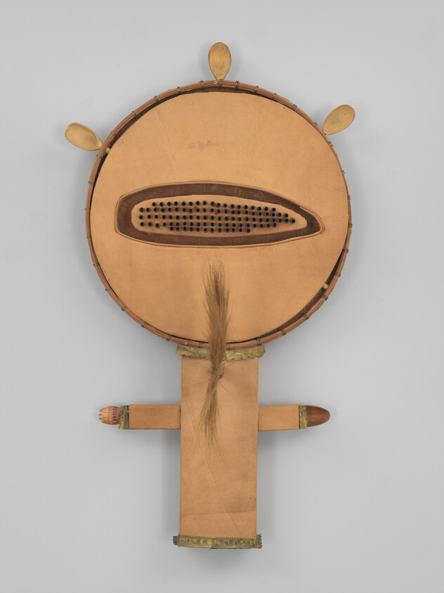 Large circular mask with a central perforated mouth, leather straps, and a horsehair tuft.