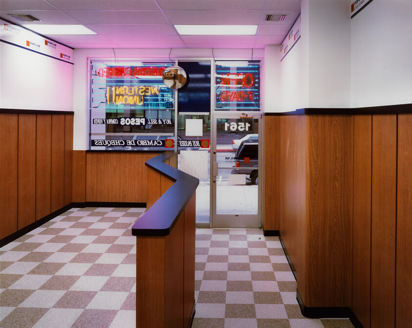 Empty storefront with zigzag counter, wood-paneled walls, checkered floor, and neon open sign.