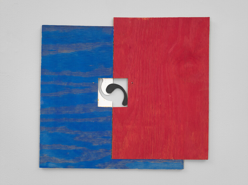 Two overlapping wooden panels, one blue and one red, with a small cutout showing a black curved shape.