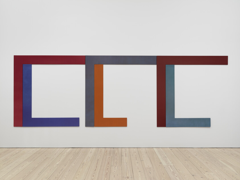 Three large, colorful L-shaped geometric panels are arranged side by side on a plain white wall.