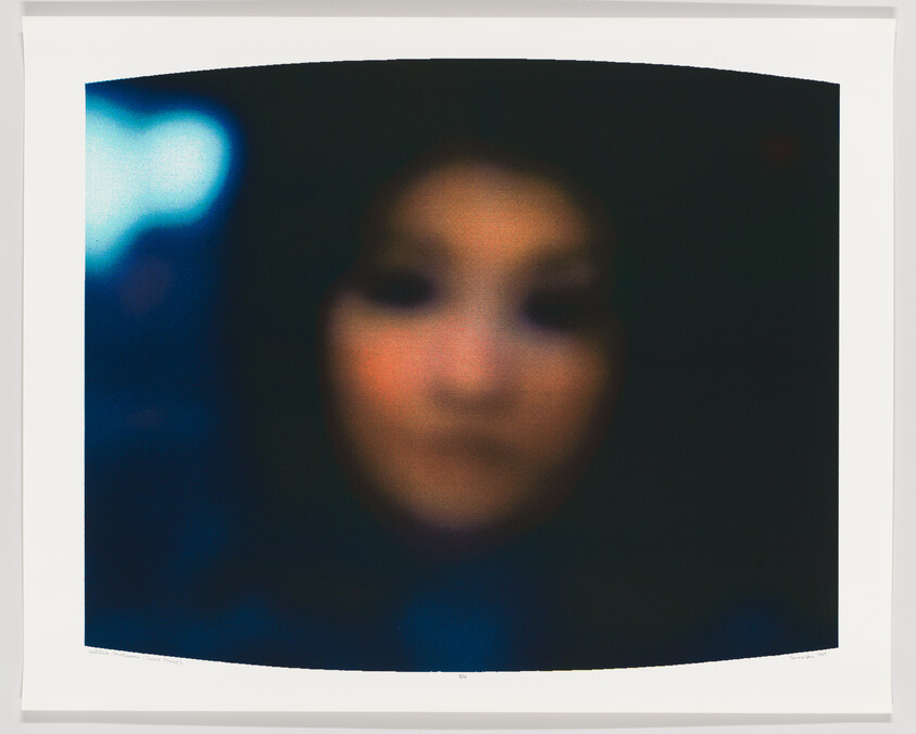 Blurry close-up of a person’s face with soft, muted colors and dark surroundings.