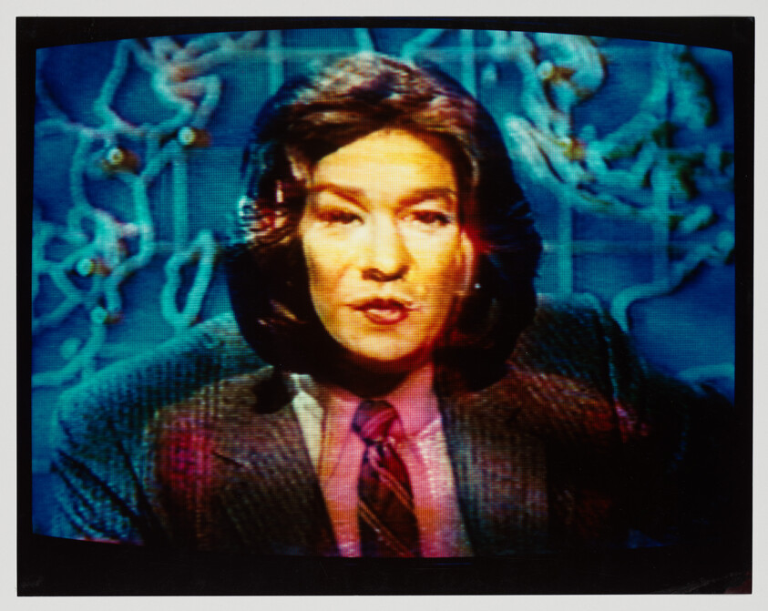 A television newscaster in a suit and tie speaks in front of a blue map backdrop.