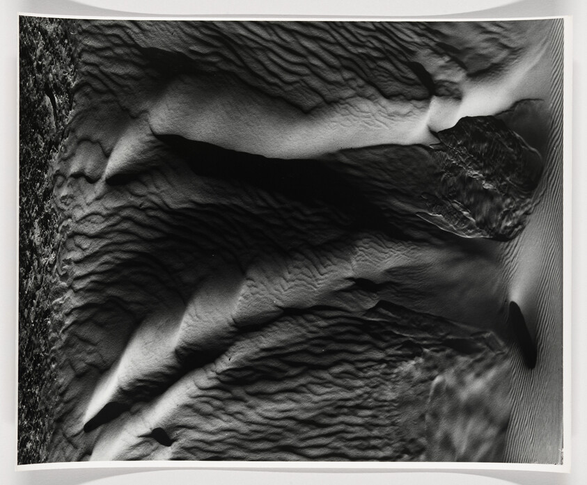 Aerial view of rippled sand dunes with deep shadows and textured ridges.