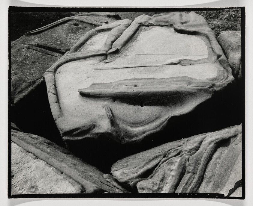 Smooth layered rocks with curved erosion lines forming rounded shapes along a rocky shoreline.