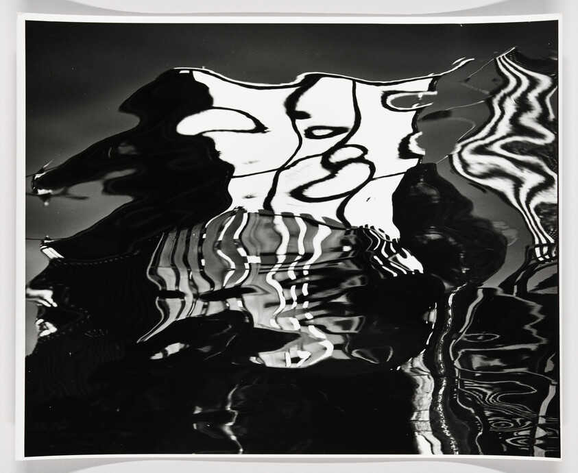 Black-and-white distorted reflections create wavy shapes and vertical stripes on rippling water.