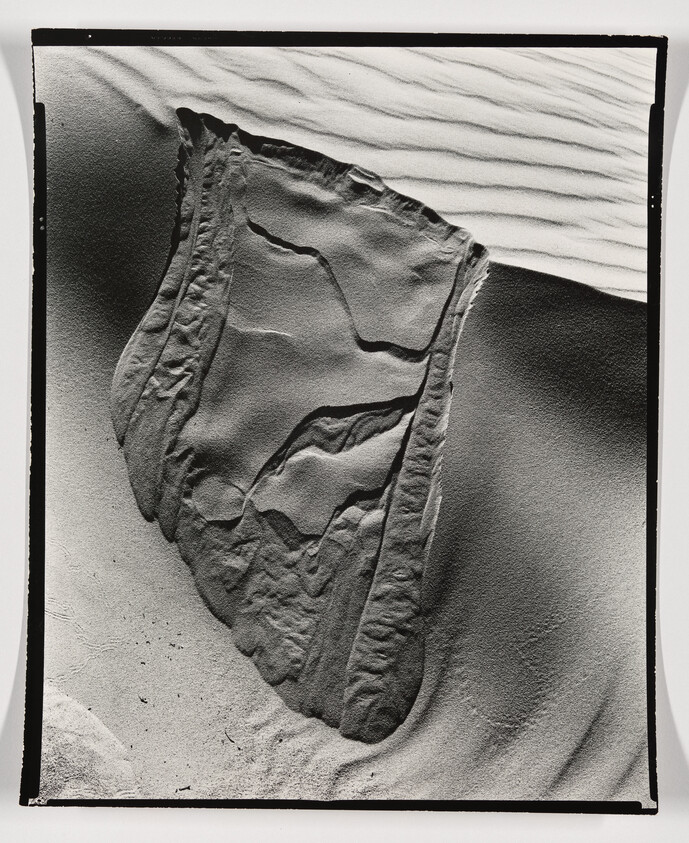 Large weathered sand slab with layered ridges and ripple patterns on surrounding dunes.