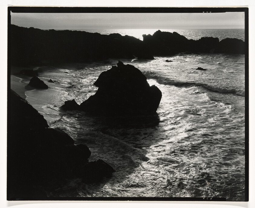 Rocky shoreline with waves crashing and sunlight reflecting off the water.