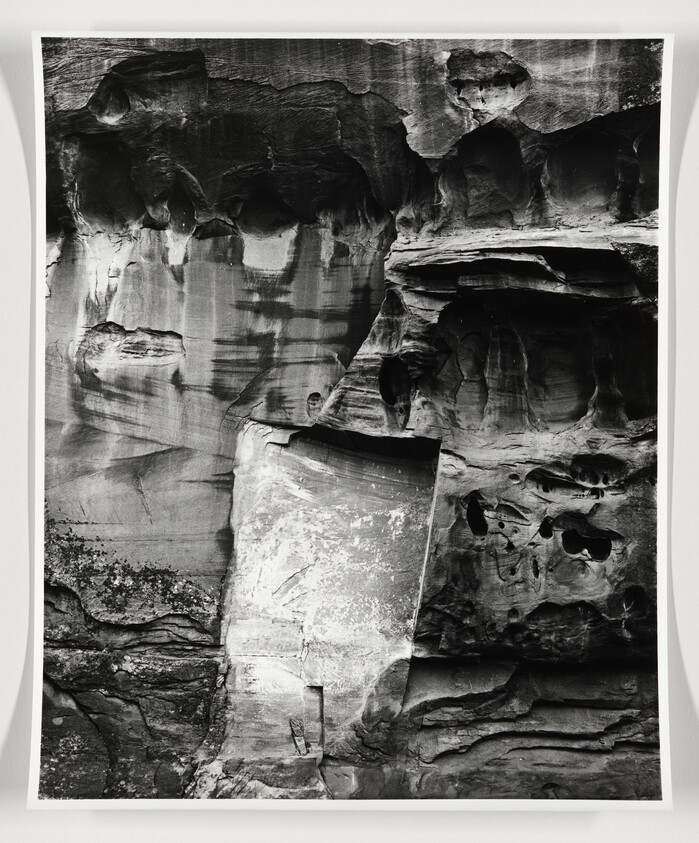 Tall layered rock cliff with smooth erosion patterns and rounded cavities in black-and-white.