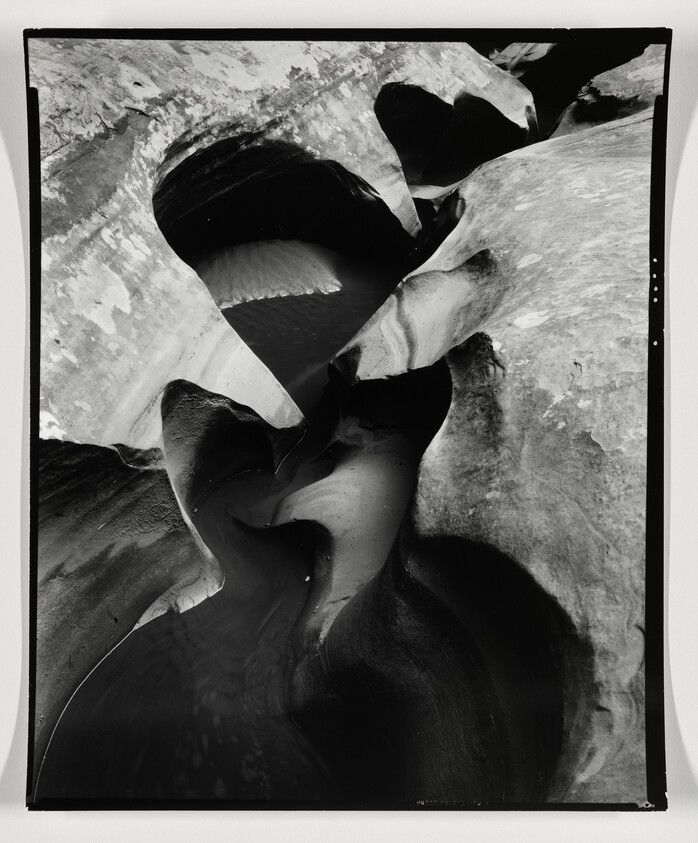 Smooth, curving rock formations and shallow water pools carved into a narrow, winding canyon.