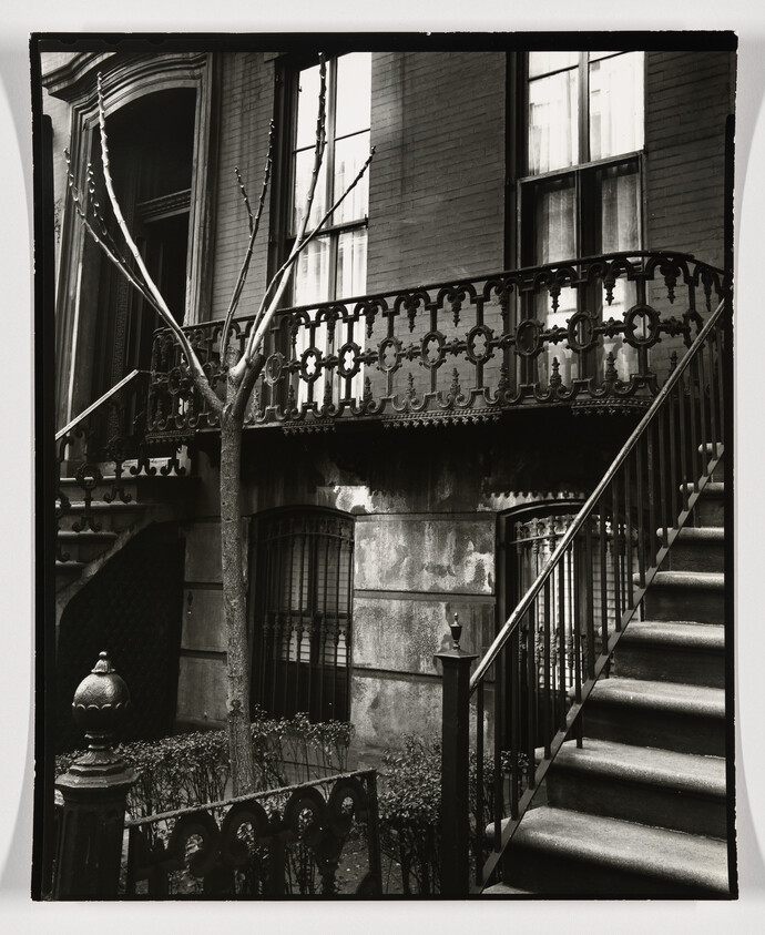 A stone stoop with ornate iron railing and steps leading to a brownstone entrance.