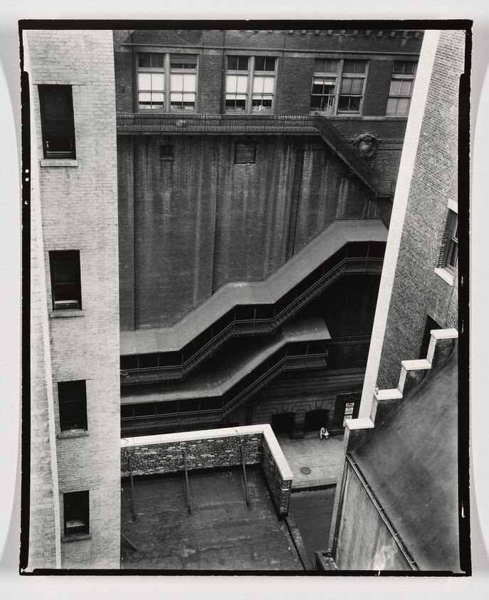 Three-tiered metal emergency stairways zigzag down the side of a tall brick building above an alley.