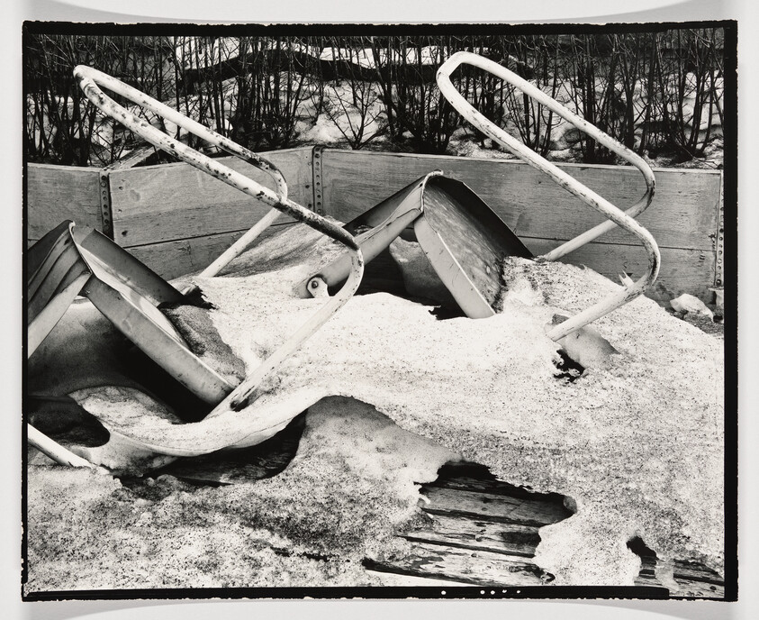 Two overturned metal sleds with bent handles partially buried in snow and ice.