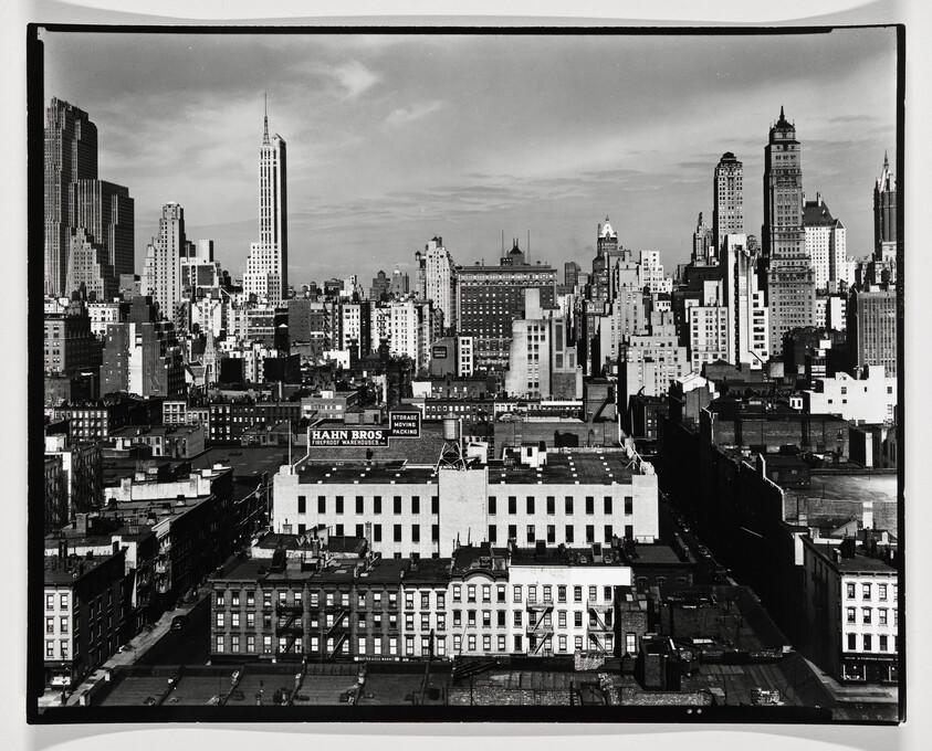 A wide black-and-white city skyline with dense mid-century buildings and a tall Art Deco skyscraper.