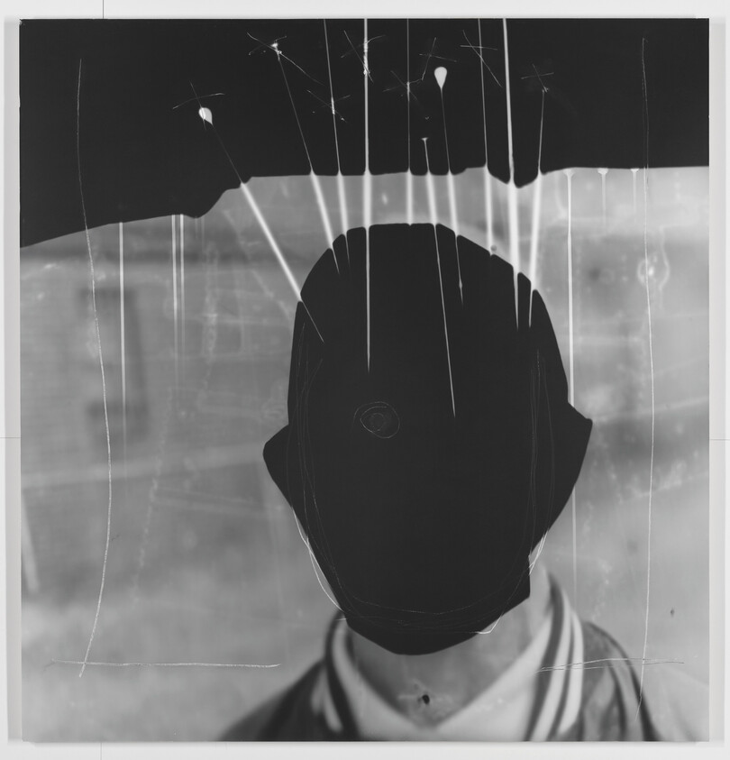 Person wearing jacket with face obscured by dark paint and white drips on the surface.