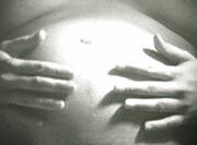 Hands gently resting on a pregnant belly, highlighting the shape and curve of the stomach.