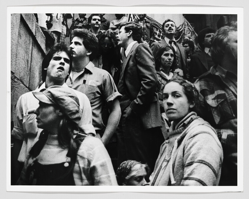 A crowded group of people on stairs look upward with serious, determined expressions.