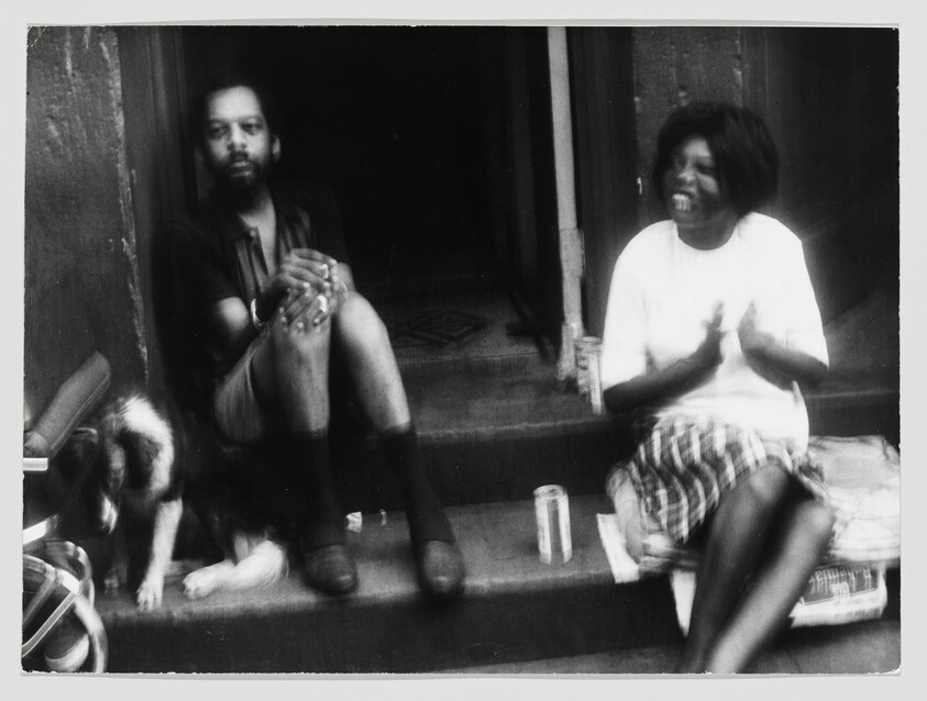 Man and woman sit on front steps with a dog as the woman claps and laughs.