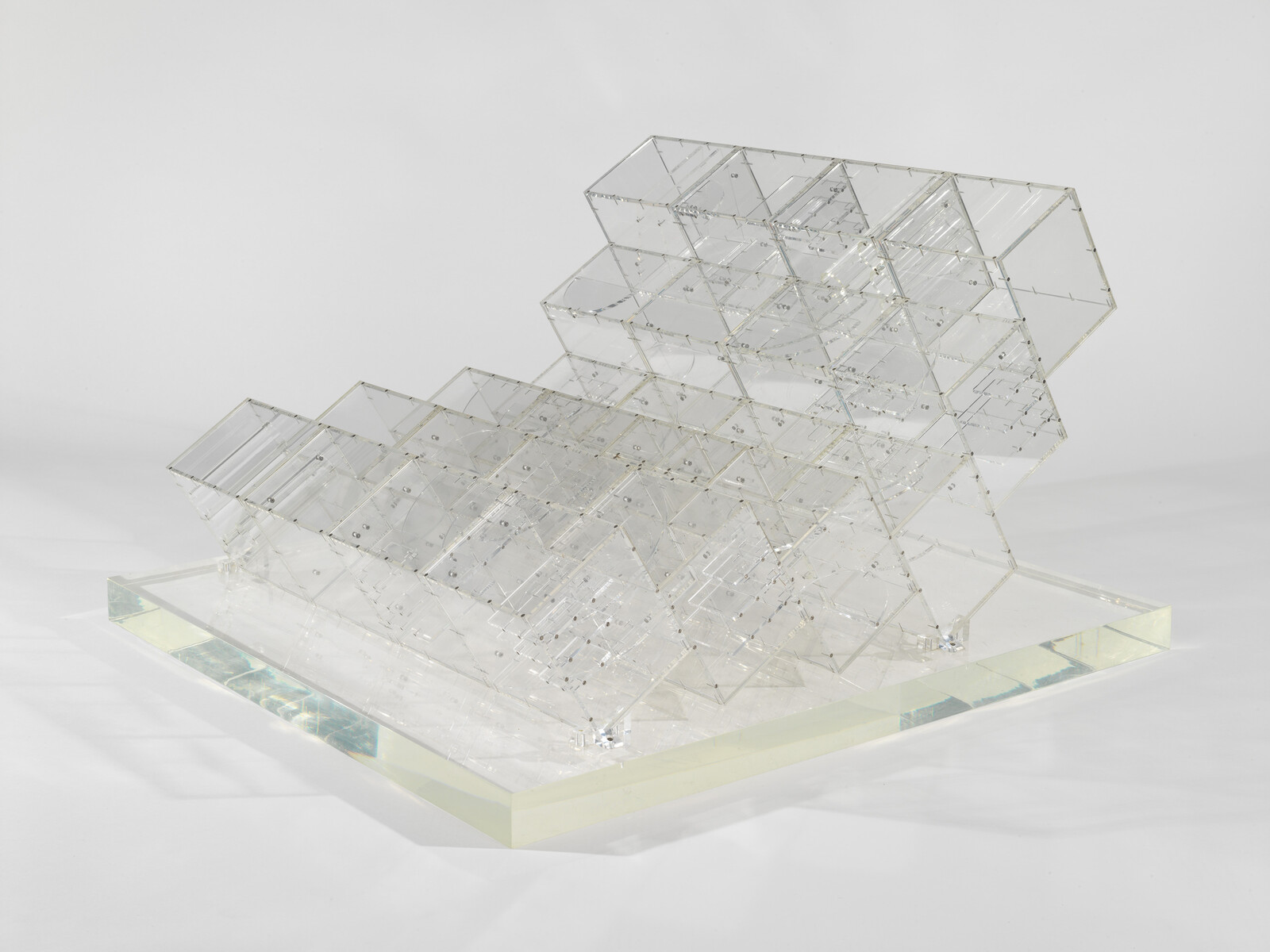 A clear acrylic sculpture of stacked transparent cubes tilted diagonally on a rectangular base.