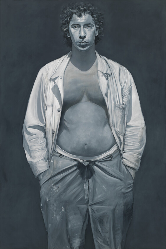 A standing man with unbuttoned shirt and hands in pockets looking straight ahead.