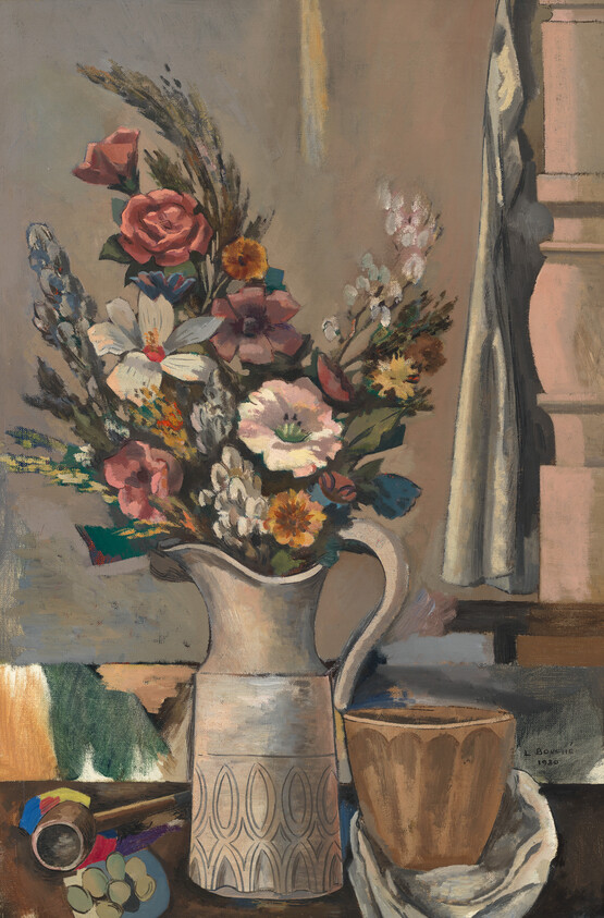 A ceramic pitcher filled with mixed flowers sits on a table beside a cup.