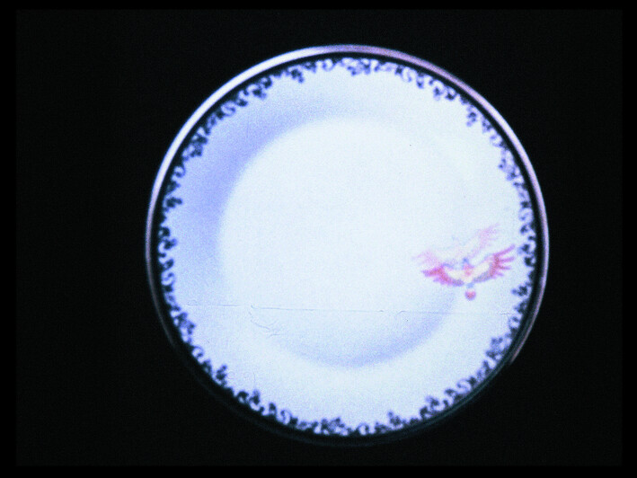 A decorative round plate with dark ornate border and a small pink bird motif on the right.