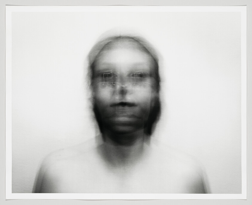 A blurred, double-exposed black-and-white portrait of a person with soft, overlapping facial features.