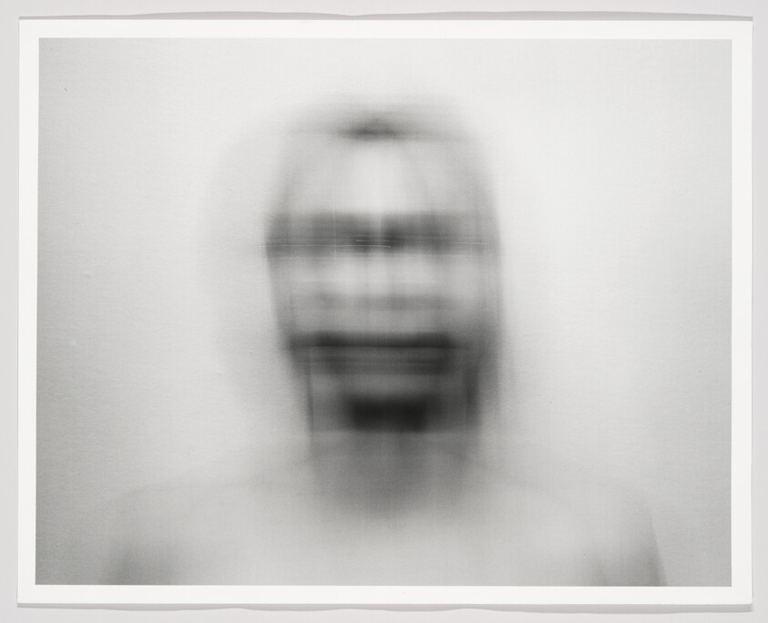 A blurred monochrome human head with vertical motion blur creating multiple facial outlines.