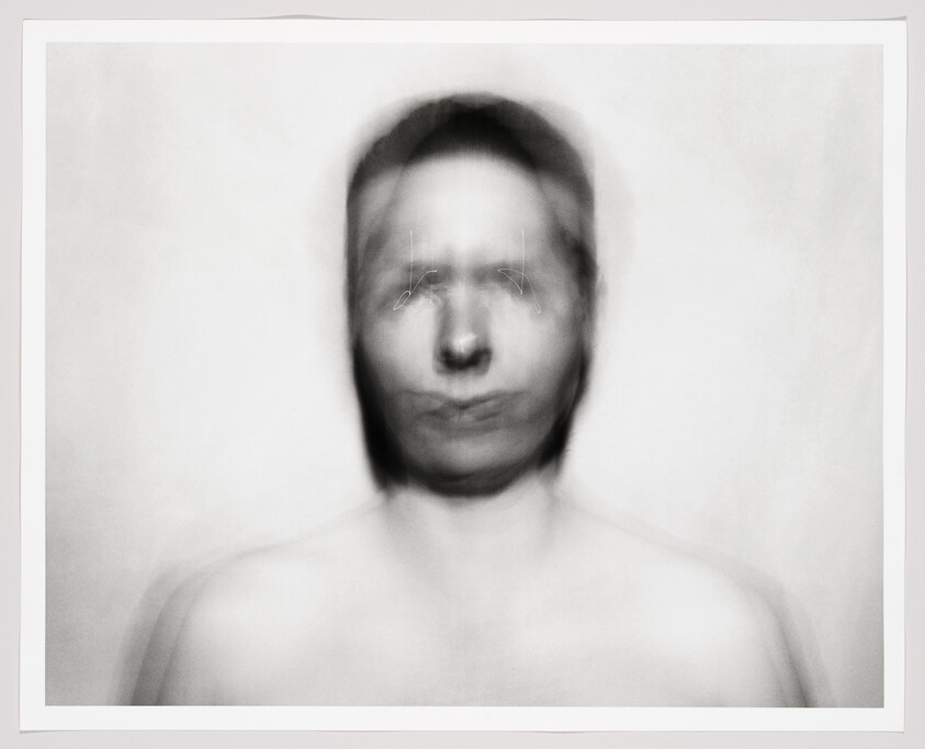 Blurred black-and-white portrait of a person with a ghostly, doubled face and bare shoulders.