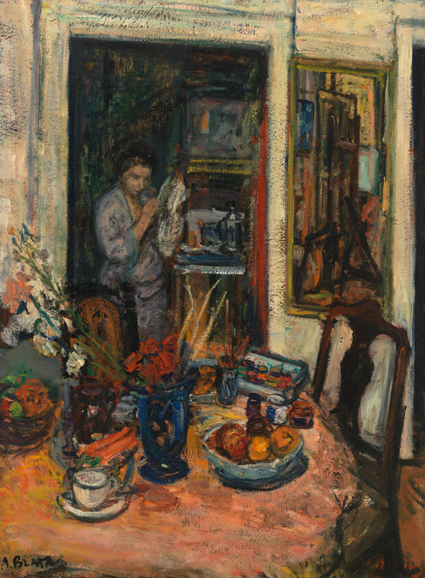 A cluttered dining table with fruit and vases while a person reads in the doorway.