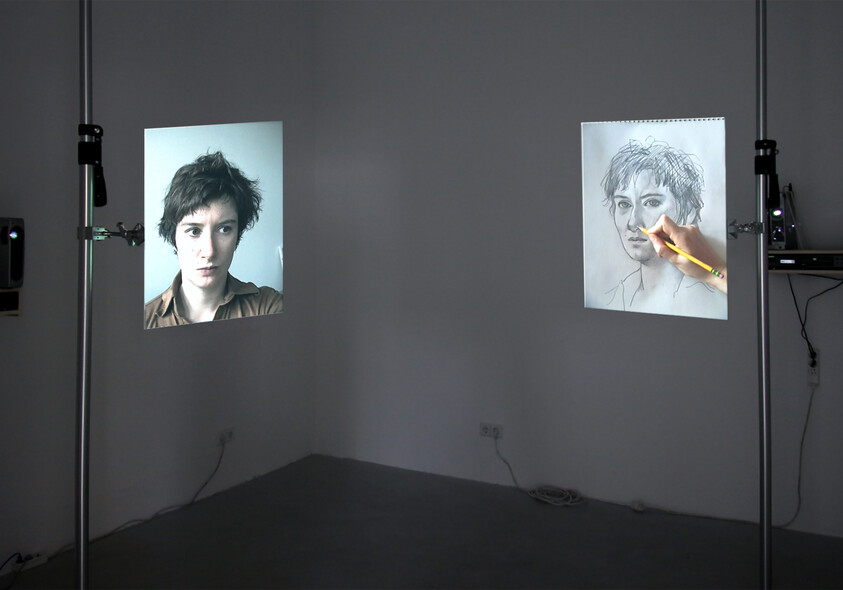 Two wall projections show a young person's portrait and a hand drawing a sketch of the same face.