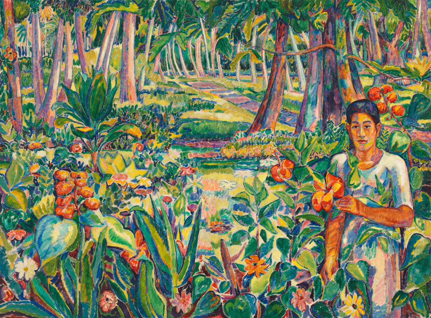 A person stands in a colorful tropical garden holding orange flowers amid dense foliage and trees.