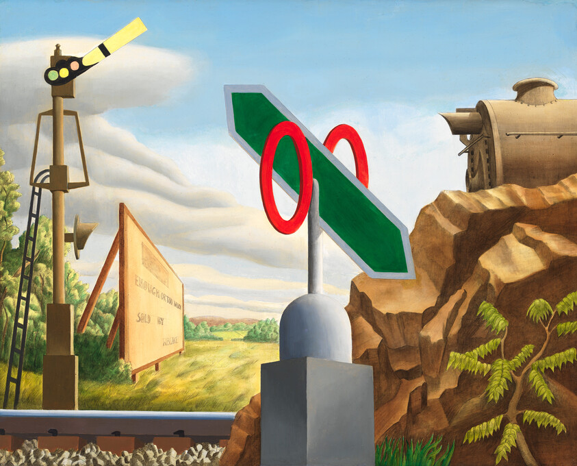 A green directional sign with two red rings stands beside railroad tracks and a rocky hillside.