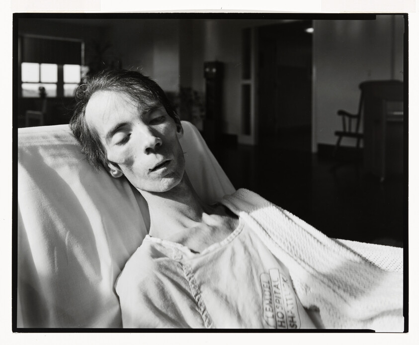 A frail hospitalized person lies back in a bed, eyes closed and head tilted to one side.