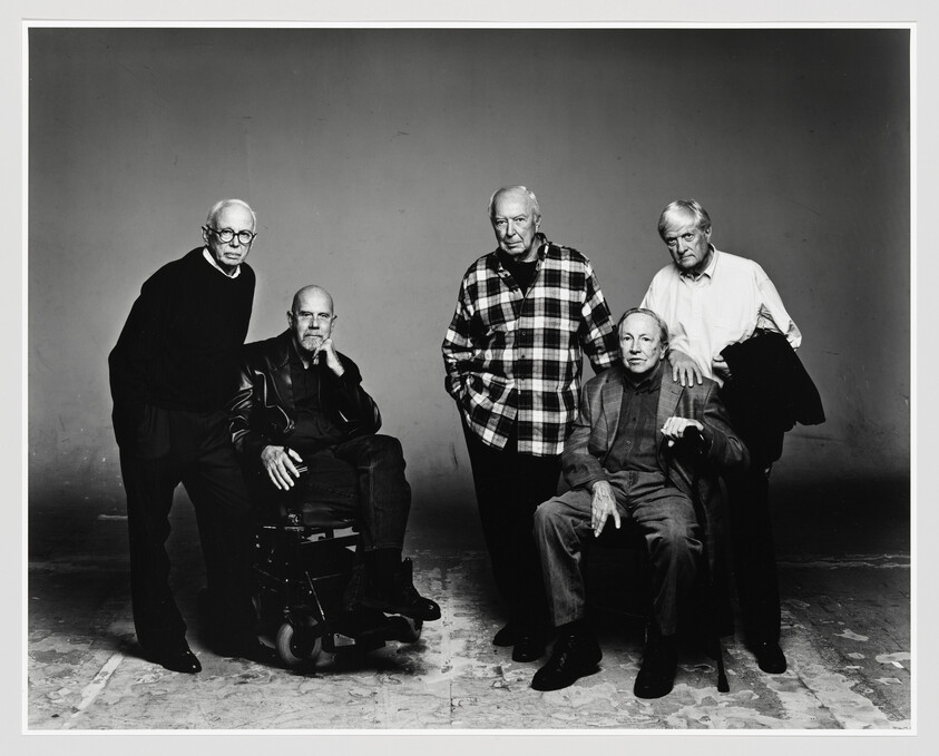Five older men pose together in a studio, two seated and three standing with casual expressions.