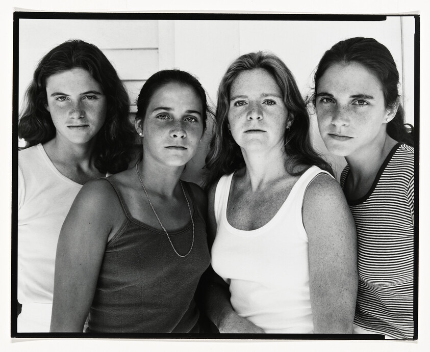 Four women stand close together facing the camera with serious expressions.