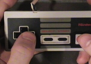 Two hands holding a vintage Nintendo controller, thumbs pressing the D-pad and buttons.