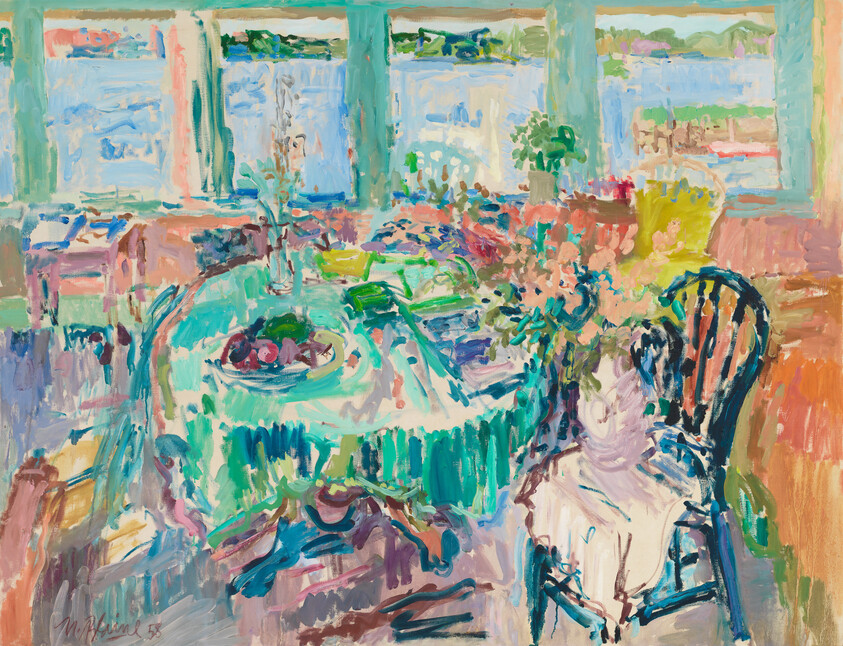 Sunlit dining table with fruit bowl and chair beside large windows overlooking water.