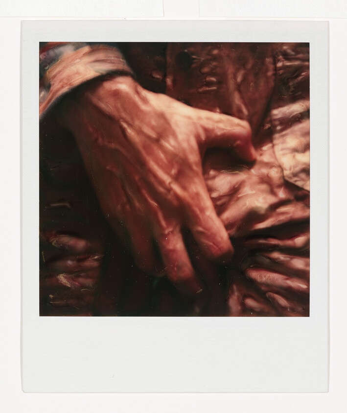 An elderly hand rests on a crinkled coat, showing visible veins and deep wrinkles.