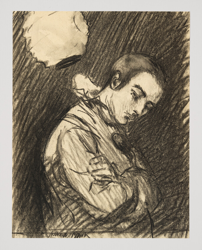 Young man in a coat sits with arms crossed, looking down under a lamp.